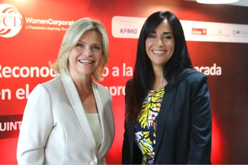 Two women smiling against a red WCD branded backdrop.