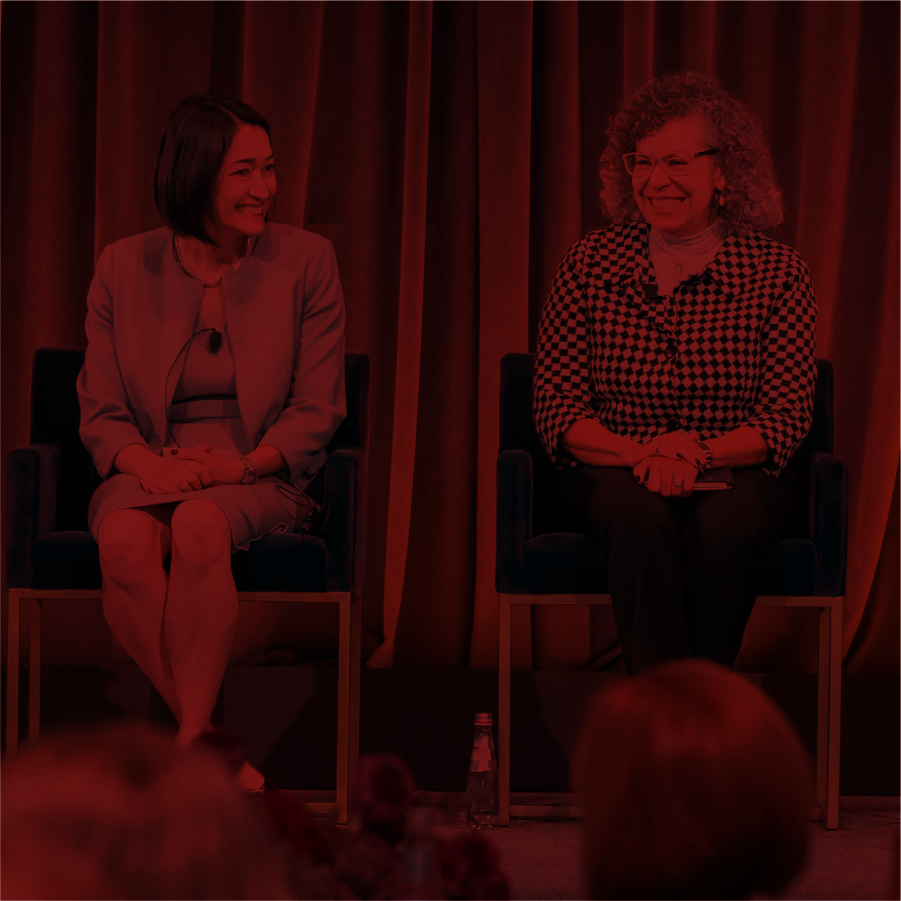 Two women panelists on a stage laughing